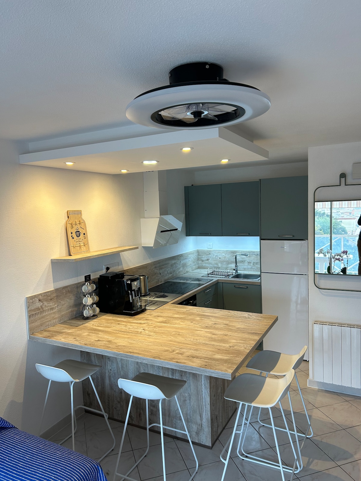 The kitchen area features a central island with three sleek stools, providing a space for casual dining. Modern appliances include a coffee machine, microwave, and stove, all complemented by contemporary cabinetry. Natural light illuminates the space, enhancing its functional design.