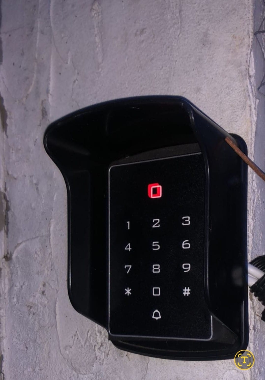 A keypad entry system is mounted on a textured wall. The keypad features a red indicator light and numbered buttons, providing a secure method for access.