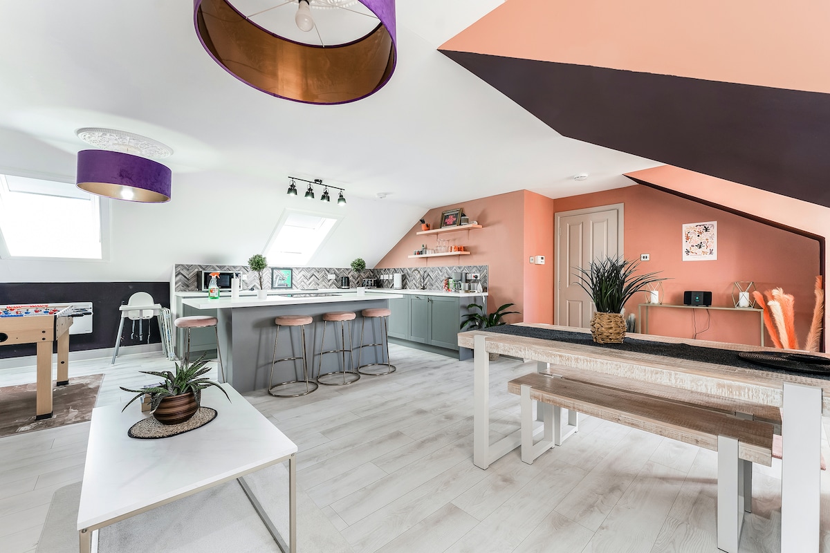 A spacious open-plan kitchen and dining area features modern cabinetry and a large island. Colorful walls in shades of peach and purple complement the stylish decor. A dining table and casual seating create a versatile space for both dining and socializing.