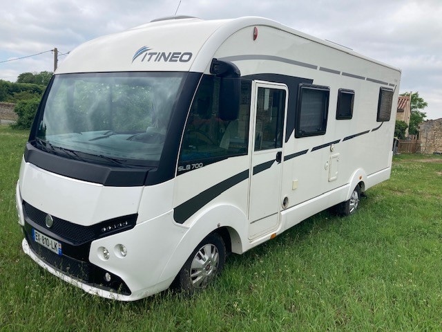 A modern camping car is positioned on a grassy area, showcasing a streamlined exterior design. Large windows are visible, providing a view of the surroundings. The vehicle features a compact yet functional layout, designed for comfort and independence.
