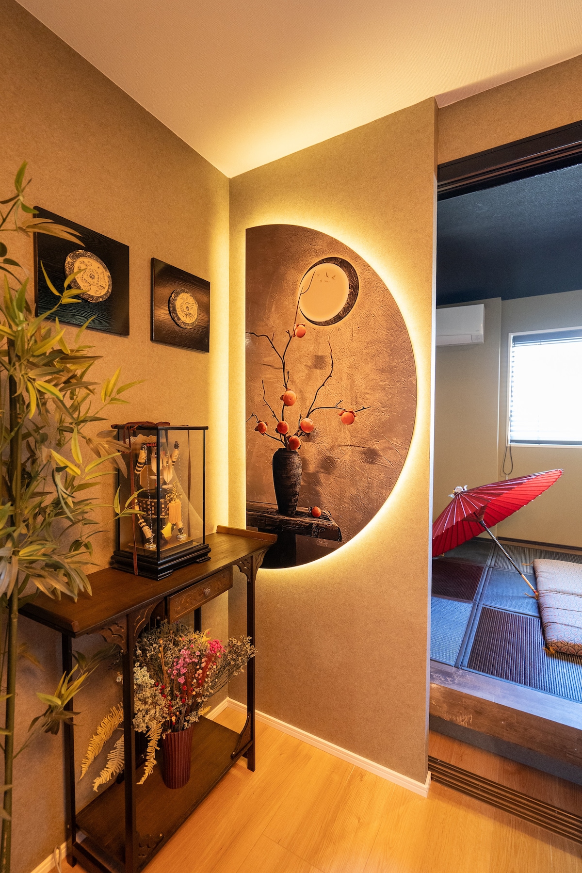The entrance showcases a serene design with carefully arranged decor, including a display cabinet and a traditional umbrella. A circular art piece with floral elements is illuminated softly, enhancing the calming atmosphere of the space.