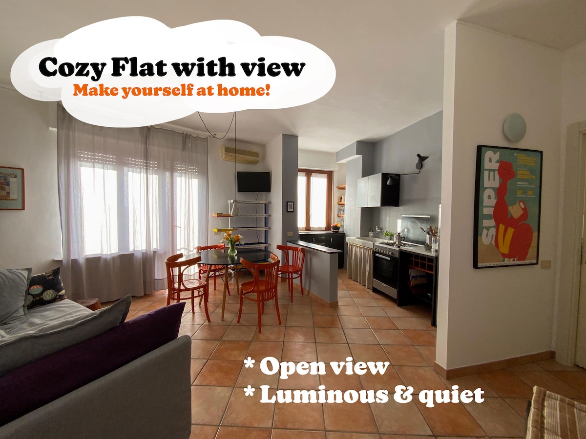 The open living space features a cozy arrangement with a spacious sofa, a dining area with four chairs, and a well-equipped kitchen. Natural light floods in through large windows, creating a bright atmosphere. The decor includes thoughtful touches, and a muted color palette ensures a calm environment.