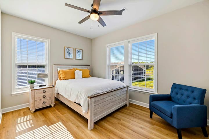 Bright bedroom with a queen-size bed, ceiling fan, and ample natural light from large windows