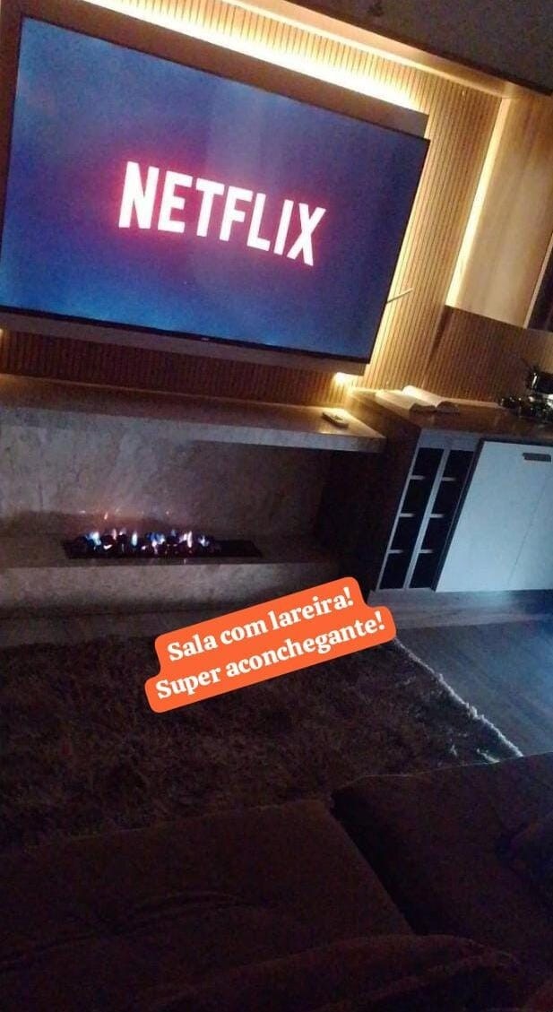 An inviting living room features a large wall-mounted TV displaying the Netflix logo. A modern gas fireplace is positioned below, providing warmth. Comfortable seating is arranged in a cozy layout, ensuring an ideal space for relaxation and entertainment.