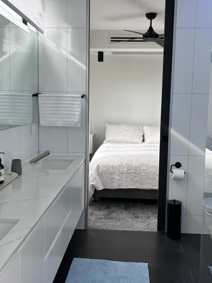 Спалната соба на горниот кат има брачен кревет (широк 150-179 см), поглед кон островот К 'Гари, клима уред, вентилатор и врска со бањата 