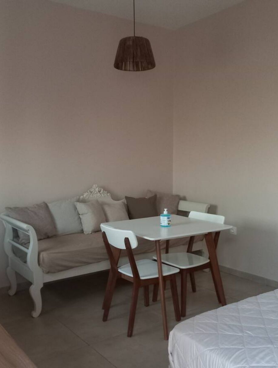 A light-colored wall is complemented by a small dining table with two chairs, positioned next to a comfortable seating area with soft cushions. A pendant light hangs above, adding a subtle touch to the serene ambiance of the space.
