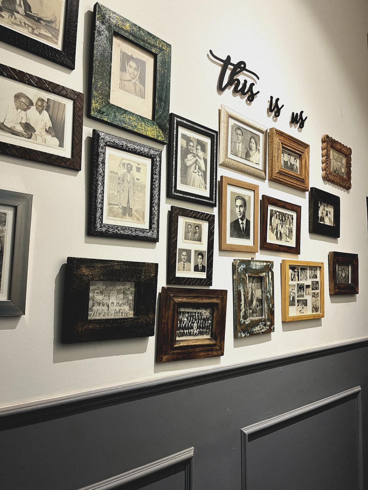 A gallery wall features an assortment of framed photographs in various styles and colors. The frames include ornate and simple designs, showcasing black-and-white and sepia-toned images. The words 'this is us' are artistically displayed at the center, enhancing the personal touch of the collection.