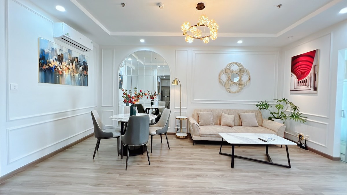 A modern living space is displayed, featuring a comfortable beige sofa and a sleek coffee table. A round dining table is surrounded by four elegant chairs. Decorative wall art and potted plants add a touch of elegance to the bright and airy environment.