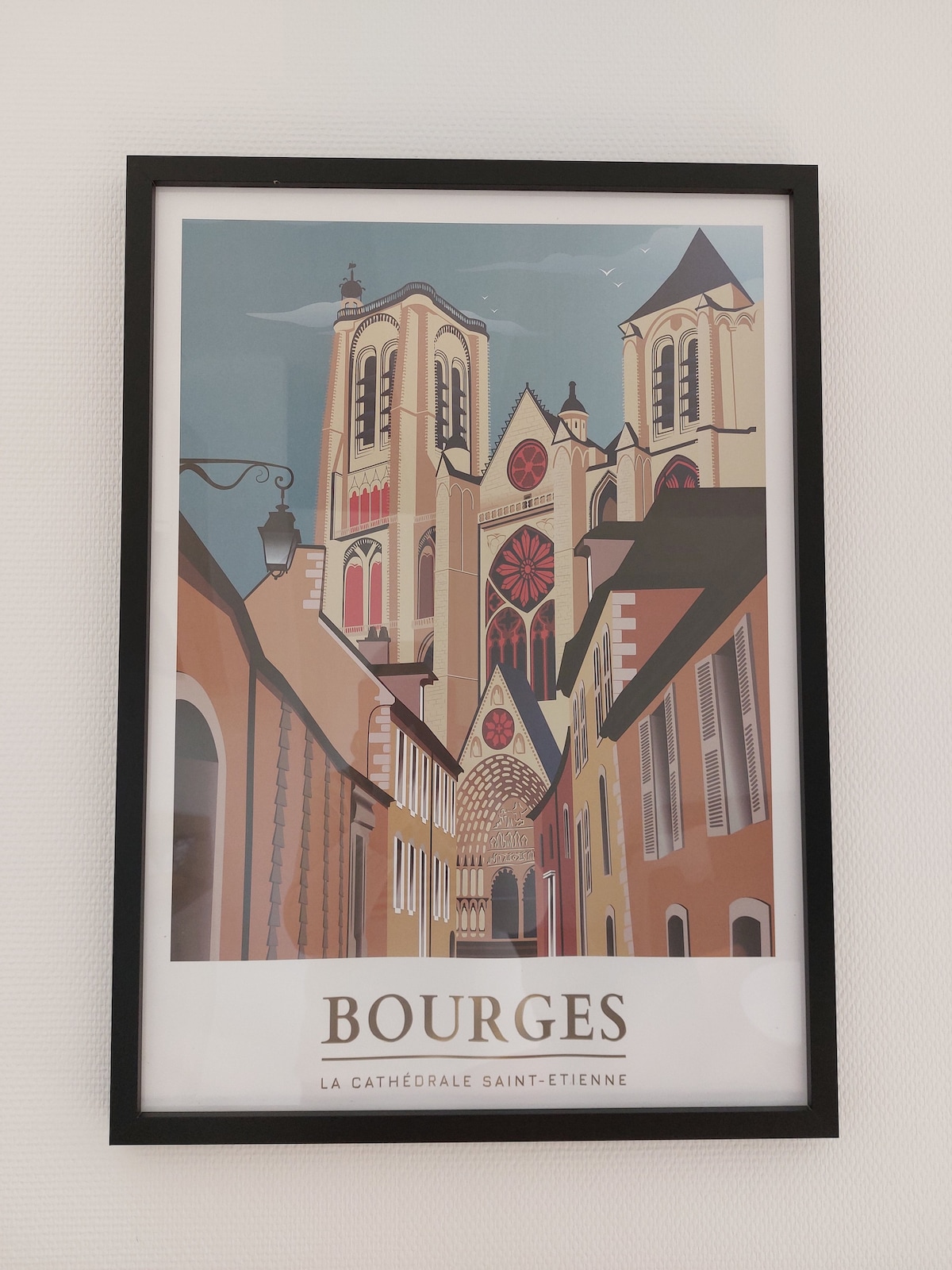A framed artwork depicting the Cathedral of Saint-Étienne in Bourges, featuring stylized architectural details and vibrant colors. The image captures the grandeur of the cathedral and the surrounding streets, conveying a sense of the city's historic charm.