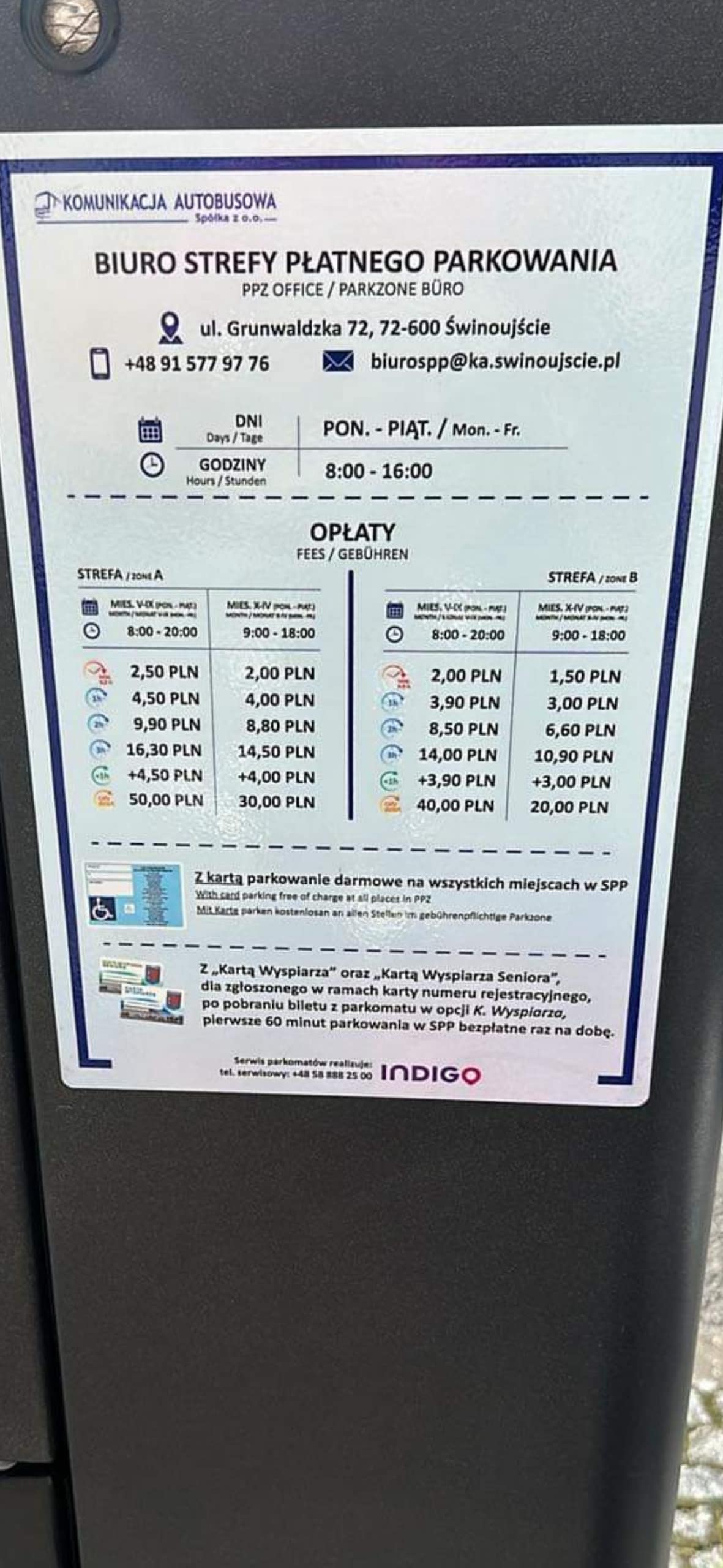 A parking information sign is displayed, detailing payment options and time schedules. The sign is printed in a clear layout with pricing and time slots listed for different days. The background appears dark, providing contrast to the white text for enhanced readability.
