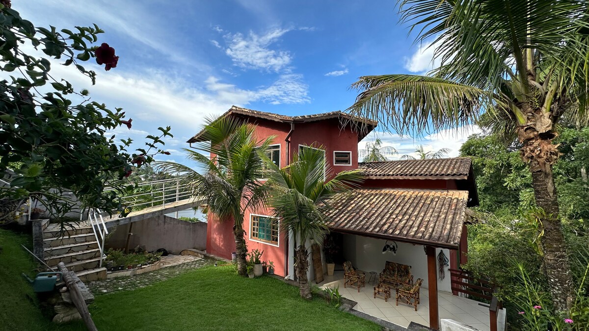 A charming two-story building is set amidst lush greenery. Palm trees frame the exterior, and a spacious patio is adorned with comfortable seating. A pathway leads to a staircase that connects to a higher level, showcasing an inviting outdoor space.