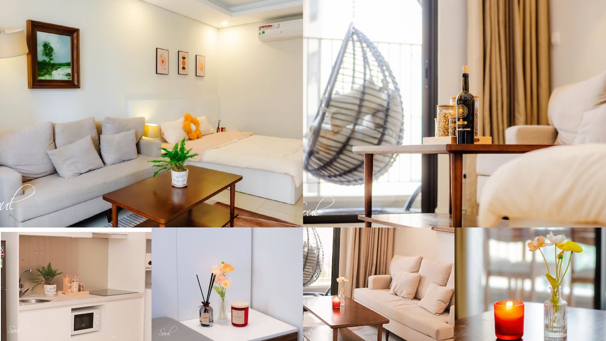 A spacious living area features a comfortable sofa, a wooden coffee table with a decorative plant, and a hanging chair. The bedroom is equipped with a large bed and soft lighting. The kitchen includes modern appliances, while flowers add a touch of color to the decor.