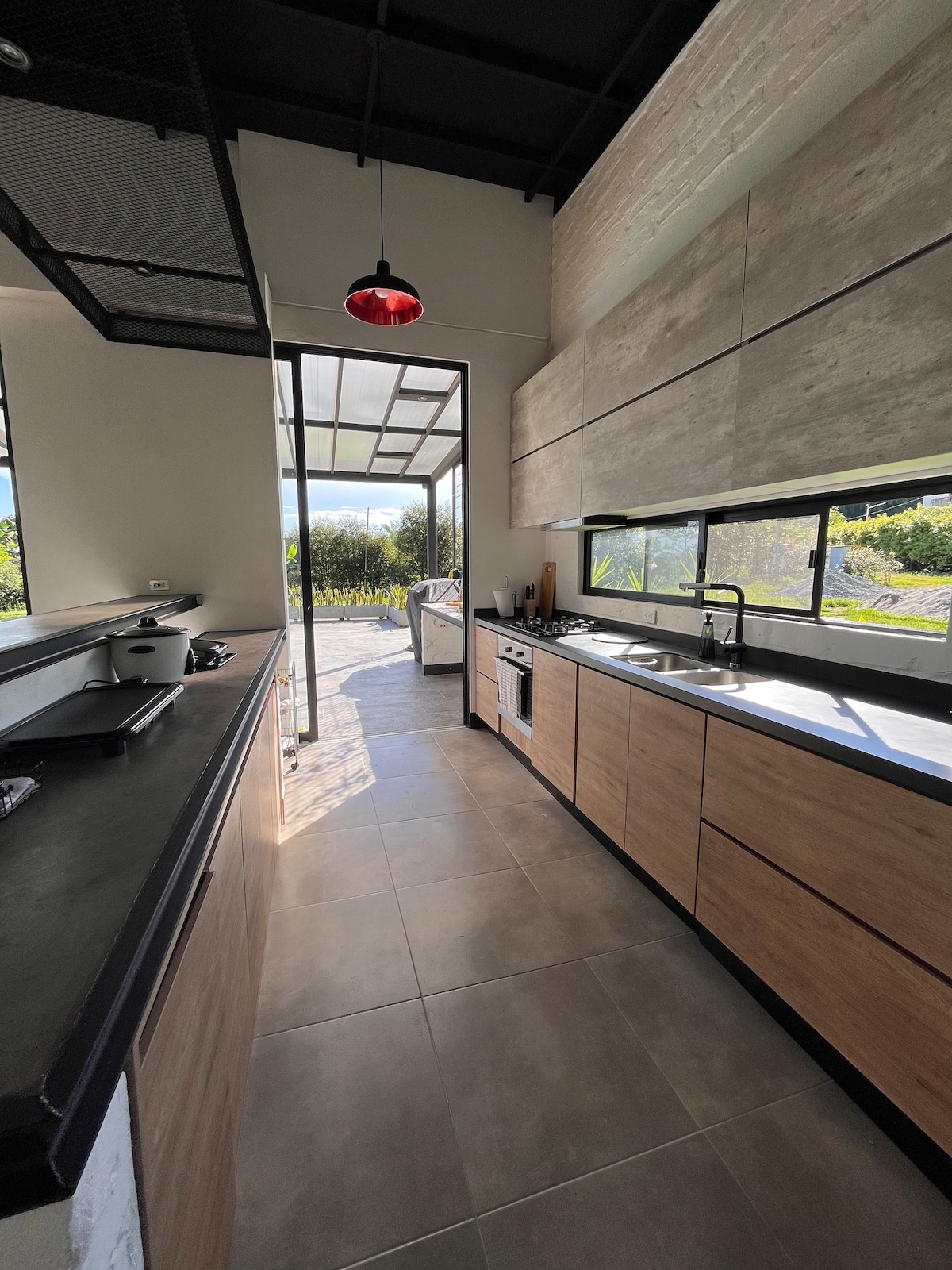 The well-equipped kitchen features sleek wooden cabinetry and modern appliances. Large windows provide views of the exterior landscape, allowing natural light to fill the space. A small island adds functional counter space, complemented by overhead lighting that enhances the kitchen's contemporary design.