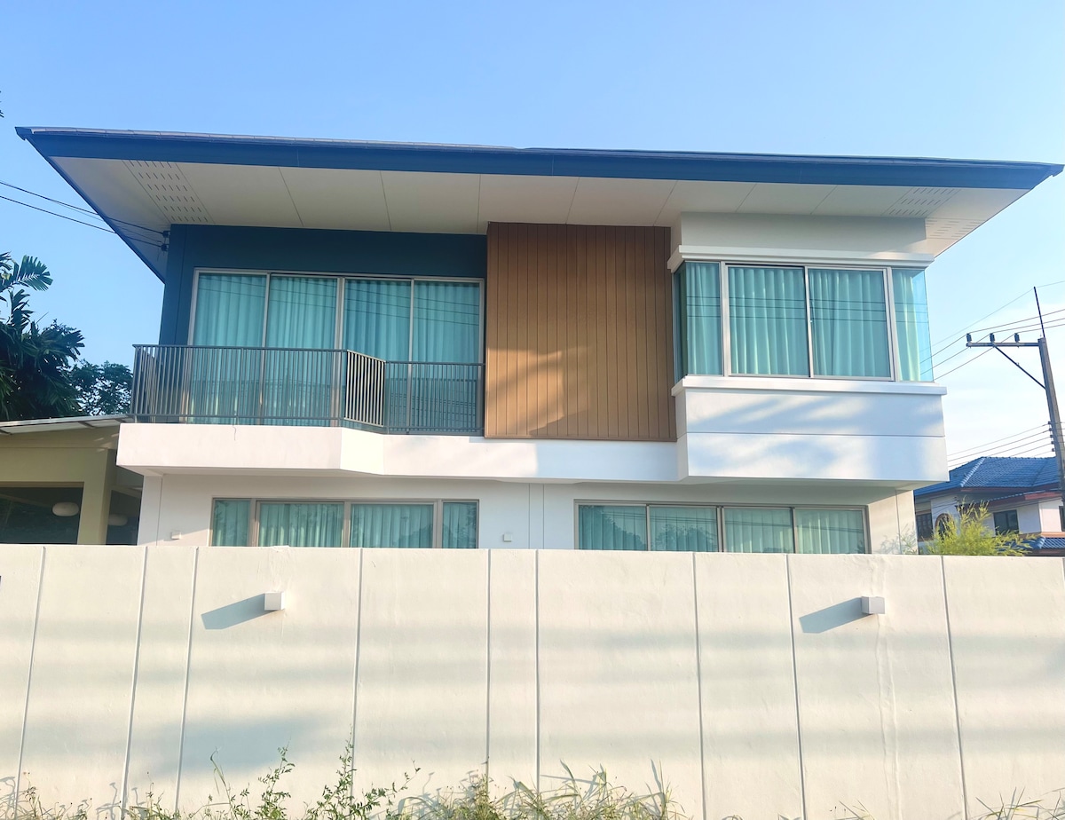 A two-story retreat features a modern facade with a combination of light-colored walls and a wooden accent. Large windows allow natural light to fill the interiors, while a balcony extends from the second floor, providing an outdoor space with a view.