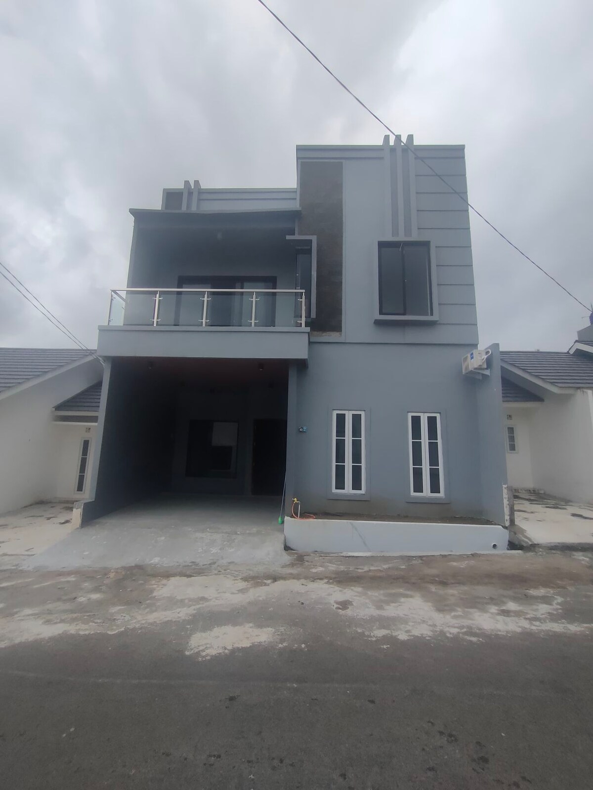 A modern, two-story house is presented, featuring a sleek grey facade and large glass doors that invite light into the interior. The structure includes a spacious entryway and multiple narrow windows, enhancing the contemporary design.