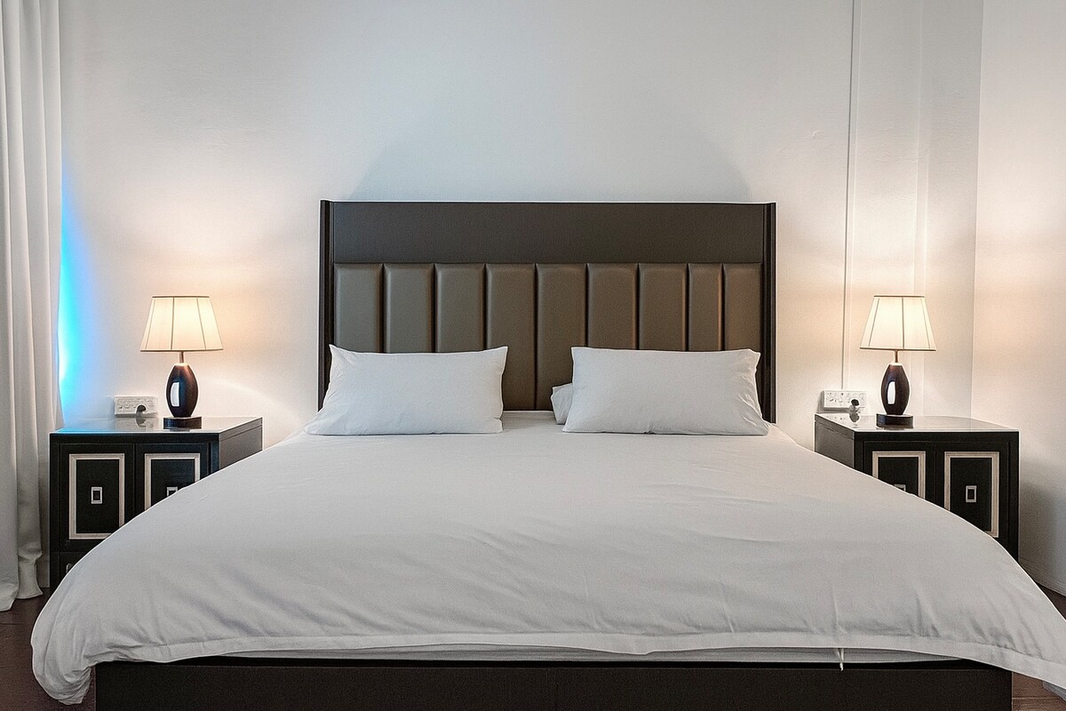 Un dormitorio tamaño king más cercano al baño, con iluminación cálida y cortina oscurecida y una vista tranquila con vistas a la parte posterior.