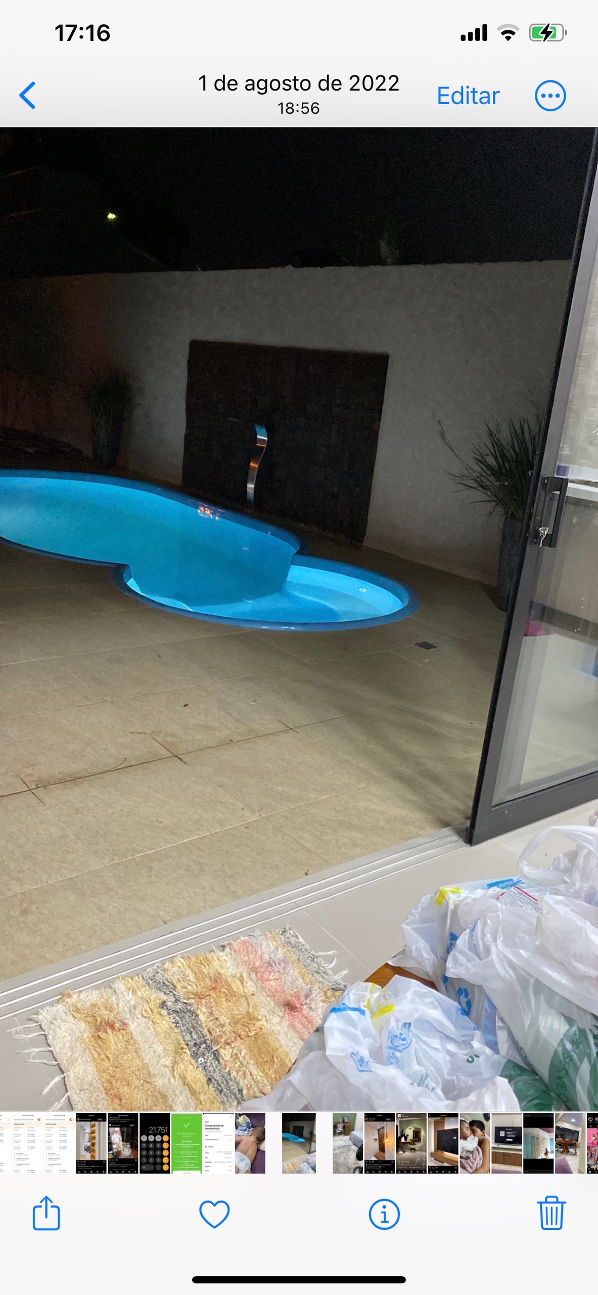 A swimming pool with an organic shape is visible in the backyard, featuring clear, blue water. Surrounding the pool are neutral-toned tiled surfaces. A wall with texture adds privacy, and plants are placed along the edges, enhancing the tranquil atmosphere.