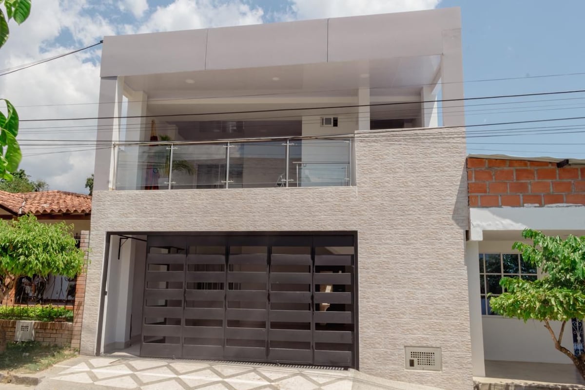 A modern two-story building showcases a combination of light-colored stone and sleek facade elements. A spacious balcony with glass railing is visible on the upper level, while the garage door below features a contemporary slatted design.