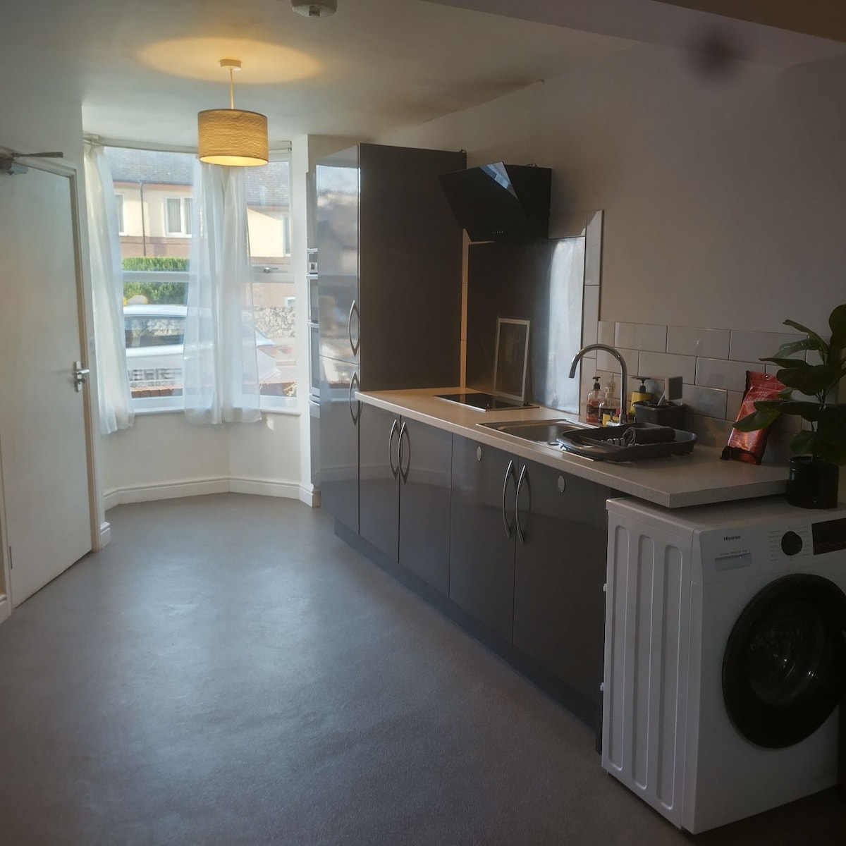 A modern kitchen area is showcased, featuring sleek cabinets with a glossy finish. Counter space is available for meal preparation, and a washer is conveniently positioned nearby. Natural light filters through sheer curtains, illuminating the room's neutral tones.