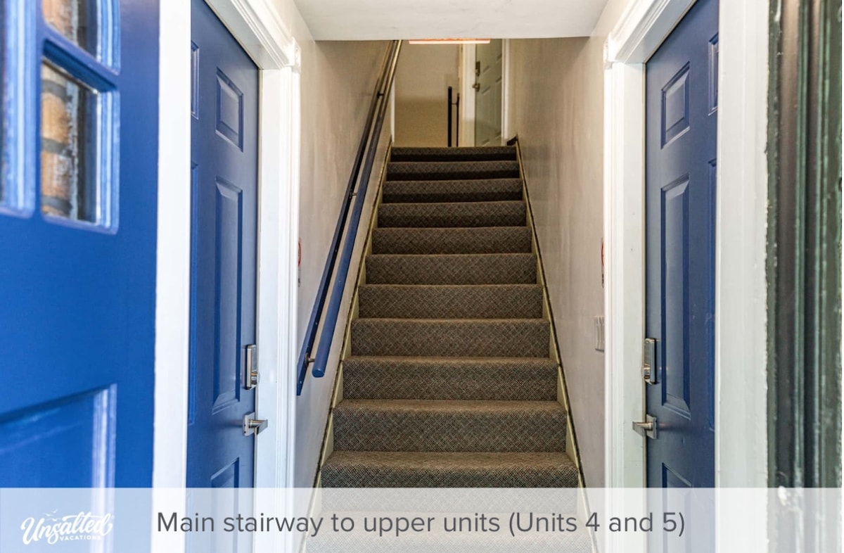 A well-lit main stairway leads to the upper units, featuring carpeted steps and a handrail for support. The doors to units 4 and 5 are painted in a calming blue color, providing a welcoming entrance to the upper level.