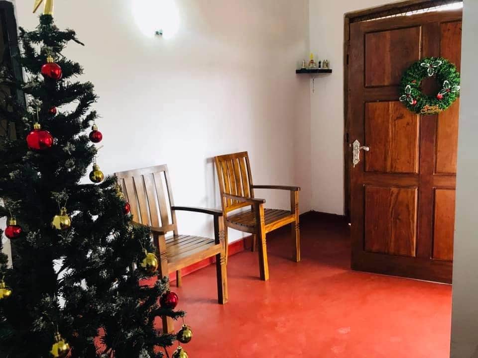 A welcoming entryway is highlighted by a festive Christmas tree adorned with ornaments. Two wooden chairs are positioned against the wall, providing a cozy seating arrangement. A wooden door with a seasonal wreath adds a touch of charm to the space.