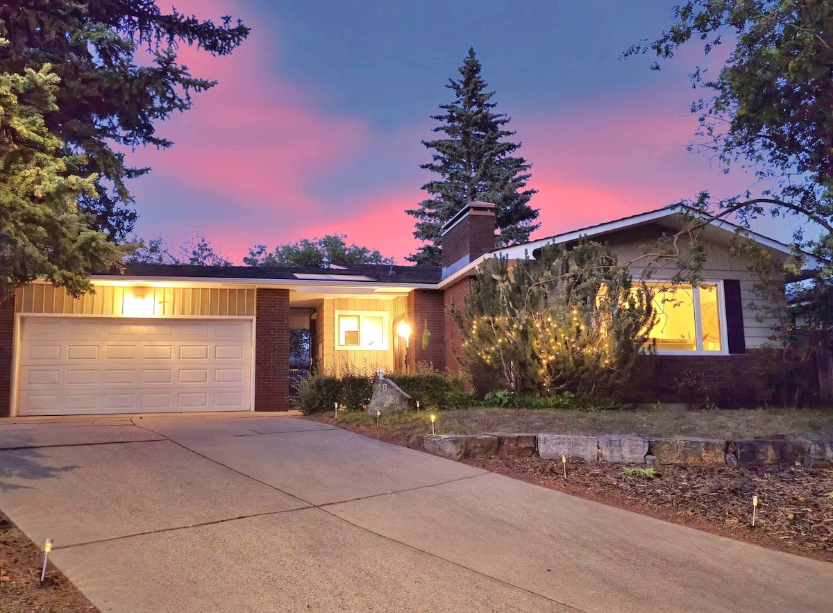 The exterior of the bungalow is displayed at twilight, featuring a driveway leading to a garage. Soft lighting from the windows highlights the welcoming entrance, surrounded by mature trees and shrubs. A serene sky filled with hues of pink and purple sets a tranquil ambiance.