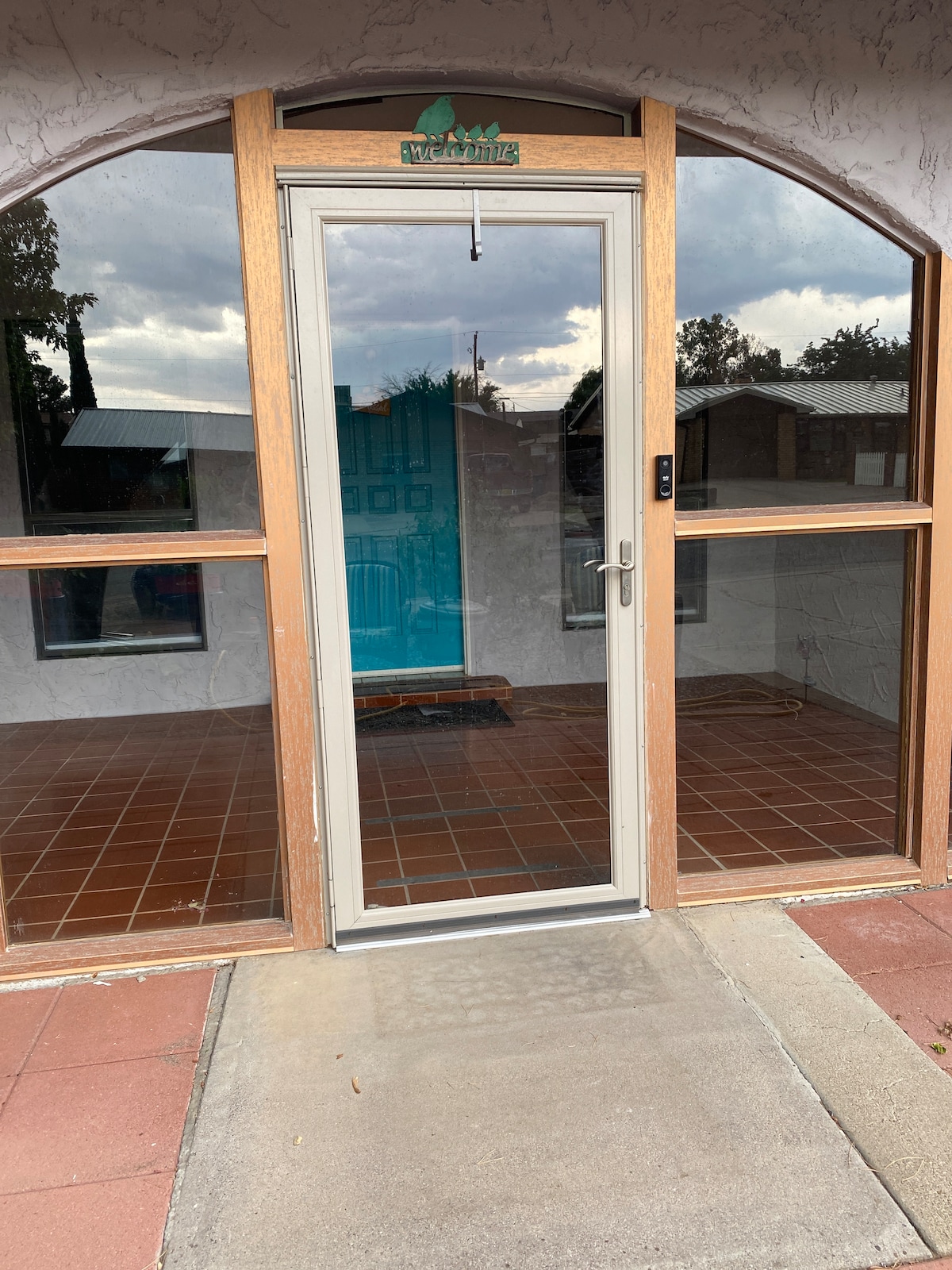 The entrance features a glass door framed by wooden panels, offering a view into the home. The tiled floor is visible, complemented by the arched design of the entryway, which allows natural light to fill the space.