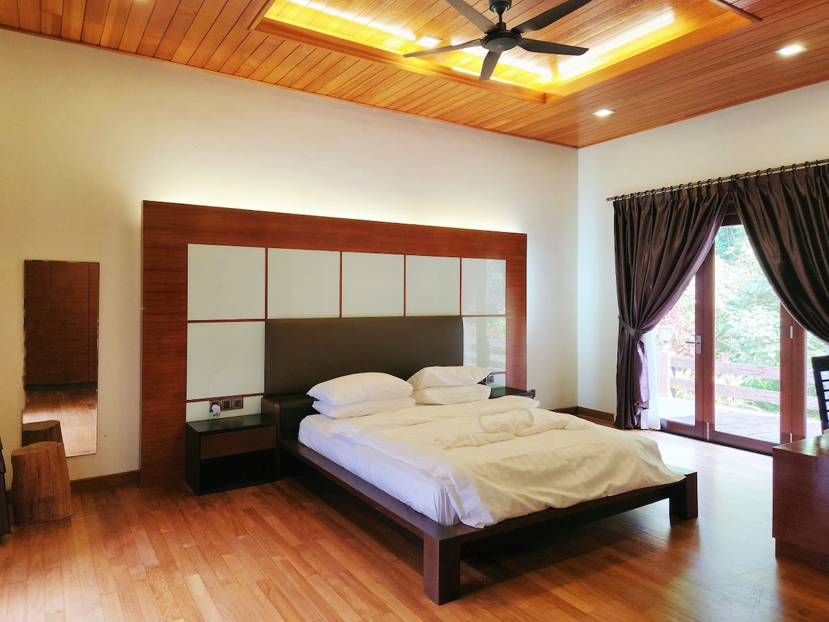 A spacious bedroom features wooden flooring and a warm wood-paneled ceiling. A large bed with crisp white linens is set against a stylish headboard. Natural light flows through the glass doors, which lead to a private balcony, while dark curtains provide additional privacy.