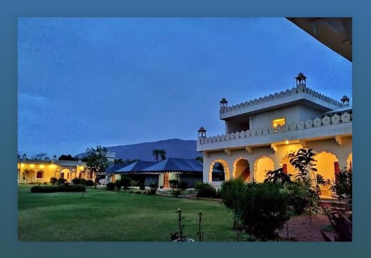 An elegant property is set against a dusky sky, showcasing intricate architectural details and well-maintained gardens. Soft lighting highlights the arched doorways and windows, while surrounding greenery adds to the serene atmosphere.