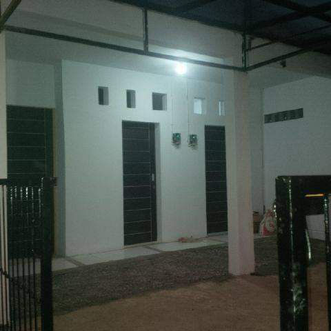 The exterior view shows a clean, modern building facade with simple lines and multiple doorways. Windows are positioned above the doors, allowing for natural light. A gravel pathway leads to the entrances, framed by a black fence that provides a sense of security.