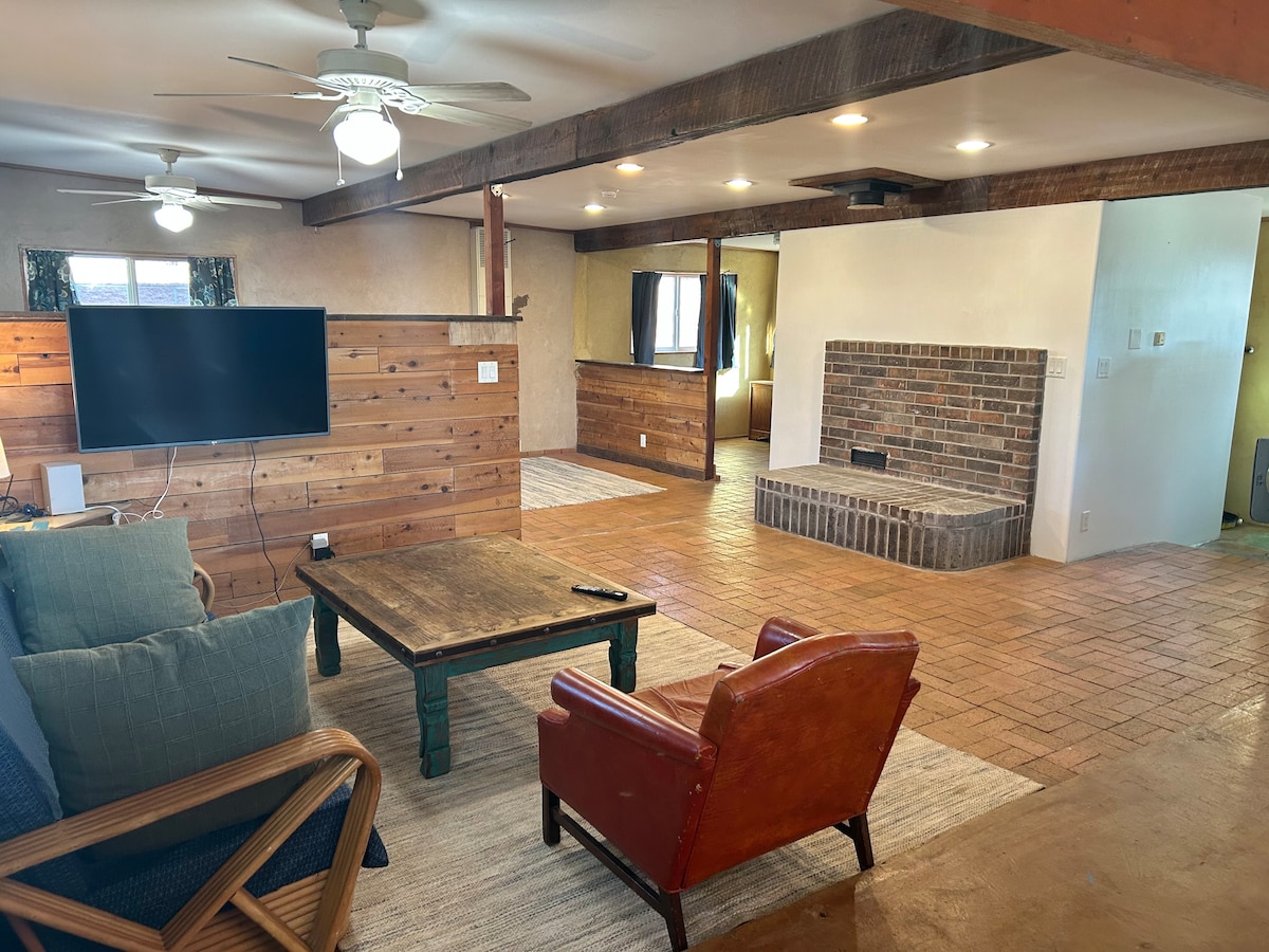 A cozy living area is presented with a mix of wooden accents and a spacious layout. The seating includes a green couch and a red armchair, with a coffee table in the center. A television is positioned on a wooden feature wall, while a fireplace adds charm to the room.