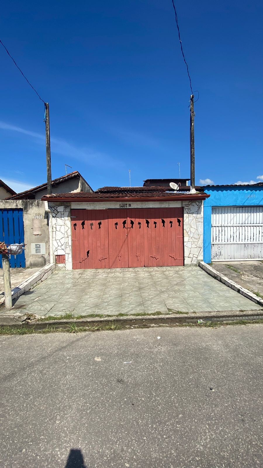 A charming exterior view of a house features a distinctive red wooden garage door adorned with patterns and flanked by stone walls. The surrounding area includes paved grounds and a clear blue sky overhead, creating a welcoming impression of the property.