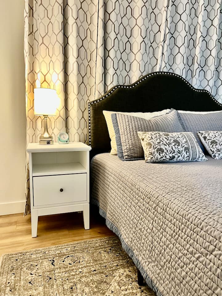 Dhomë gjumi kryesore me krevat dopio "queen" dhe abazhur tavoline anësor me portë karikimi USB dhe orë alarmi. 