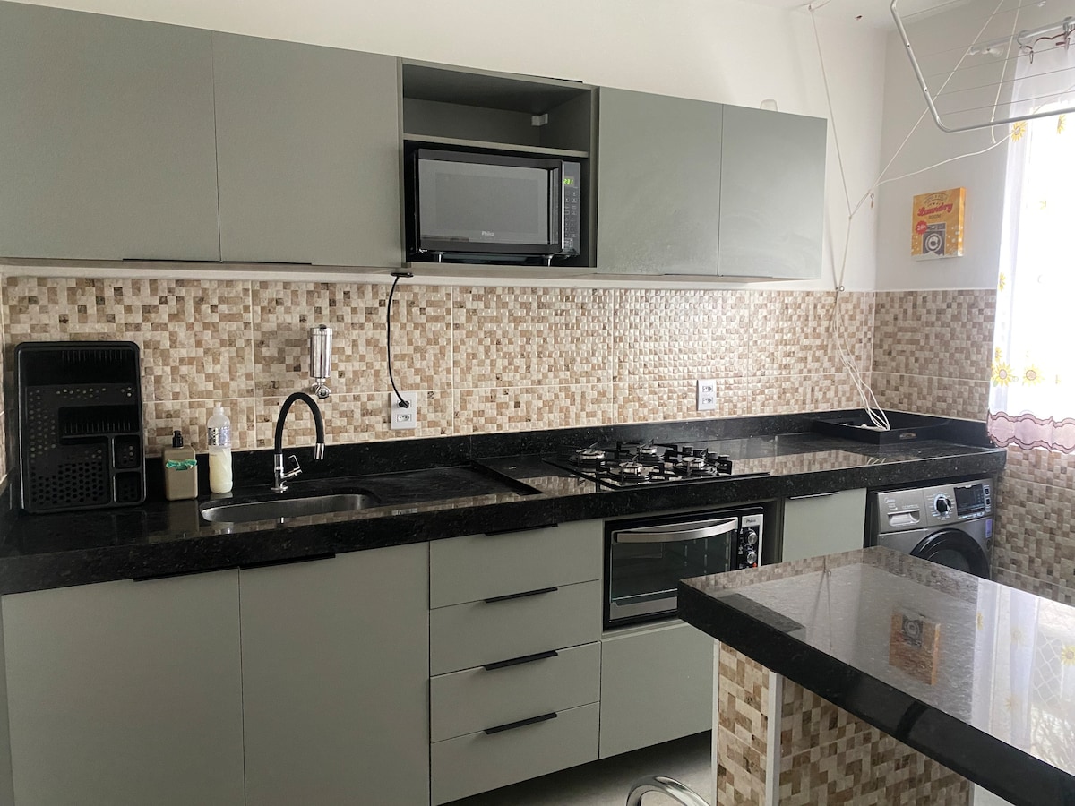 A modern kitchen area features sleek cabinetry and a dark granite countertop. Appliances include a microwave, gas stove, and an oven, with a washing machine positioned by the wall. The backsplash is decorated with tilework, enhancing the overall contemporary design.