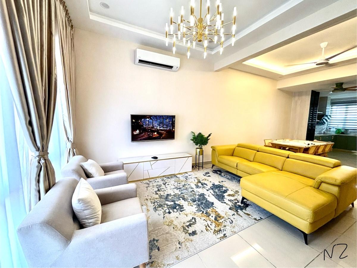 A spacious living room is highlighted by a large yellow sectional sofa and two light gray armchairs. A wide television is mounted on the wall above a white media console. Natural light enters through floor-to-ceiling curtains, enhancing the room's open feel.