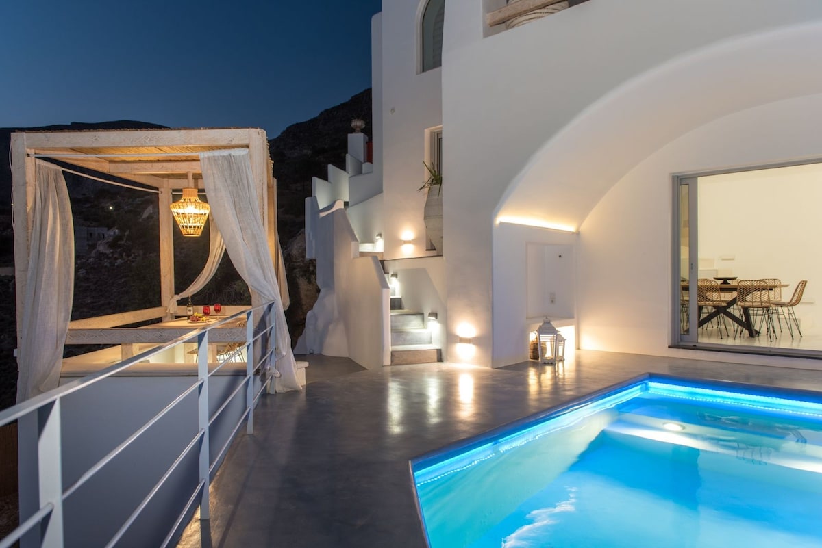 An outdoor terrace features a serene swimming pool, illuminated with soft blue lighting. A stylish canopy with sheer curtains provides a shaded seating area, while elegant lanterns line the space, contributing to a tranquil evening atmosphere.