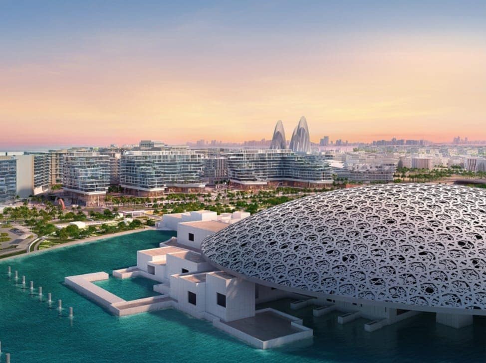 A panoramic view showcases the iconic Louvre Abu Dhabi with its unique dome architecture set against a tranquil blue water backdrop. Modern buildings can be seen in the distance, framed by a sunset sky filled with soft pastel colors.