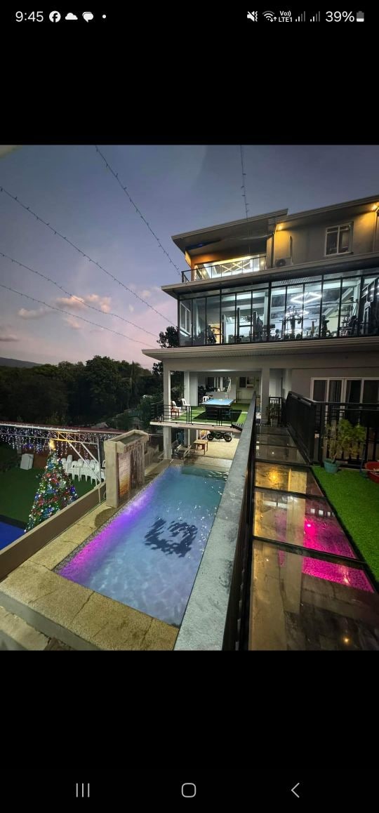 A multi-level residence features a striking outdoor pool illuminated with vibrant lighting. A spacious deck provides a view of the well-maintained garden and an event space. The structure's large glass windows reflect the twilight sky, inviting an atmosphere of openness.