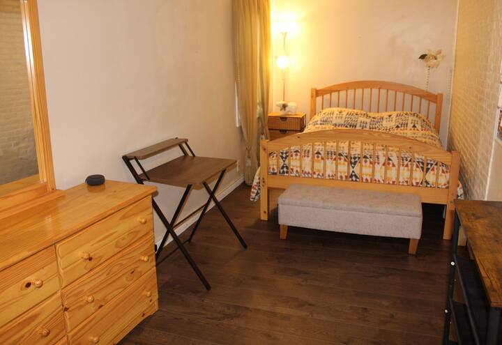 Amplio dormitorio con cama tamaño queen, cómoda, mesita de noche, zapatero, escritorio y dispositivo Alexa. 