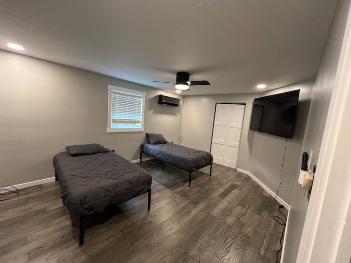 Comfortable bedroom with two separate twin beds, a wall mounted TV, and ample floor space. A great setup for children, teens, friends, or guests who prefer separate sleeping arrangements.