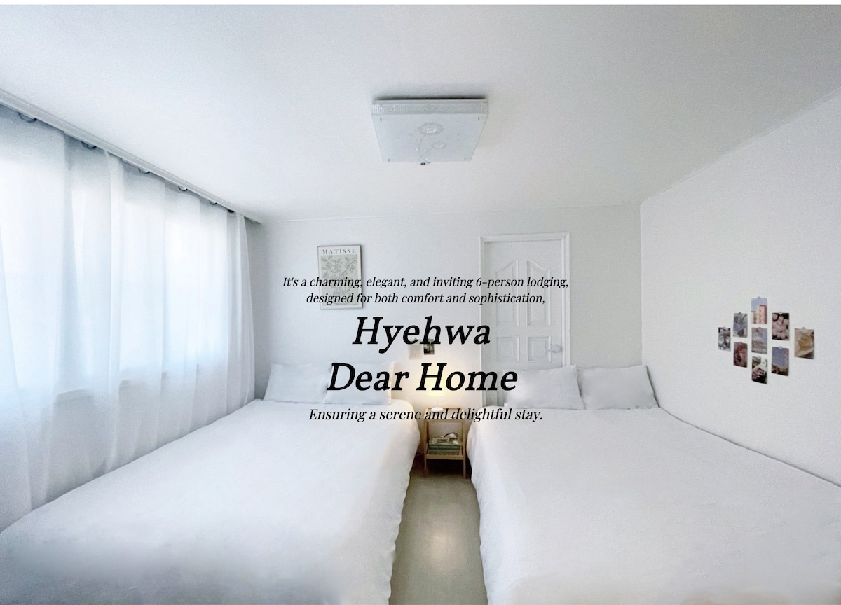 A bright and minimal sleeping area features two queen-sized beds with soft white linens. Natural light filters through sheer curtains, illuminating the simple decor. Wall-mounted photos add a personal touch, complementing the calming atmosphere.