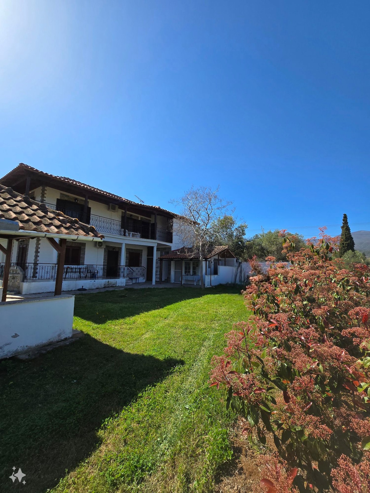 A spacious exterior view of the property is presented, featuring a two-story structure with a tiled roof surrounded by lush greenery. The well-maintained garden includes vibrant plants, contributing to a tranquil outdoor environment ideal for relaxation.