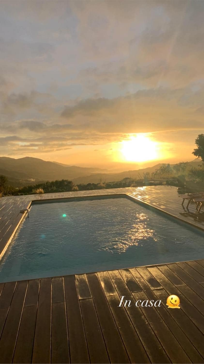 A private heated pool is set against a backdrop of mountains and a vibrant sunset. Wooden decking surrounds the pool, creating a relaxing outdoor space. The view showcases rolling hills and a tranquil sky, enhancing the overall serene atmosphere.