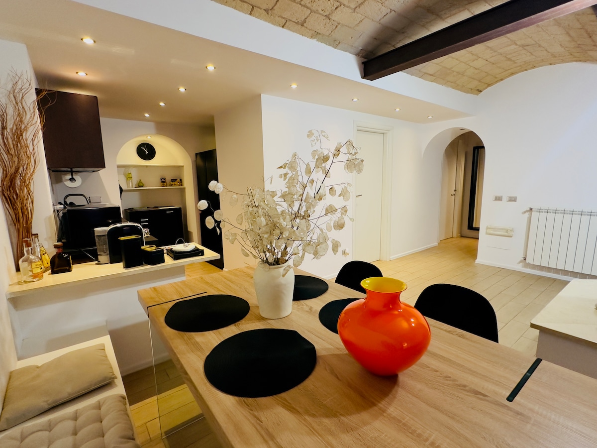 A well-equipped kitchen area features modern appliances, including a coffee maker and countertop microwave. A wooden dining table is set with black placemats and a decorative orange vase with dried foliage, enhancing the cozy dining atmosphere.