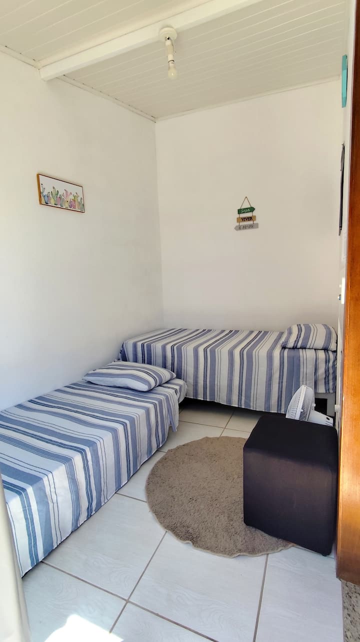 Dormitorio con 2 camas individuales, un puf y 1 ventilador 