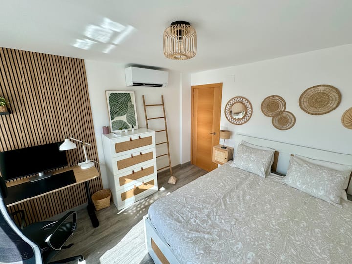 Lit queen size dans la grande chambre avec un bureau de travail dédié et un écran avec connexion USB c.