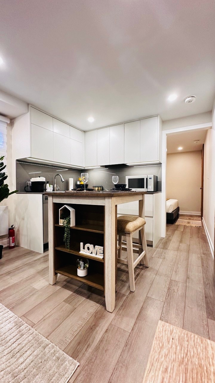 The kitchen area features modern appliances and sleek cabinetry. A small island with seating provides a space for dining. The floor showcases light wood tones, and a decorative element with the word 'LOVE' adds a subtle personal touch. A doorway at the back leads to the sleeping area.