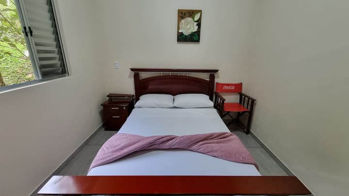 Cama de casal, cadeira de apoio, criado mudo e ventilador.