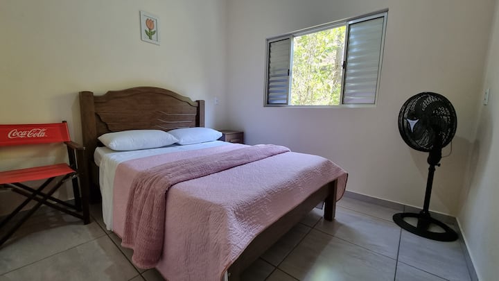 Cama de casal, cadeira de apoio, criado mudo e ventilador.