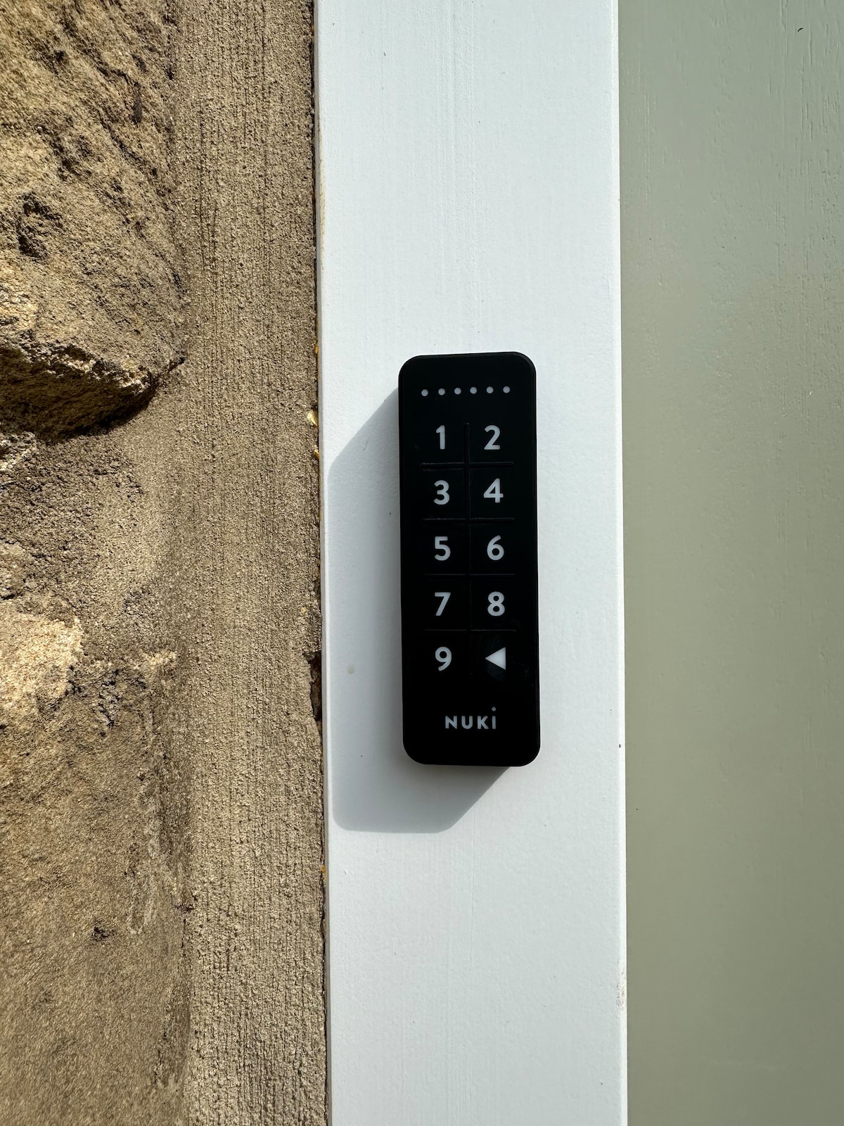 A close-up view of a keypad door entry system is displayed against a light-colored door frame. The keypad features a series of numbered buttons, allowing for secure self-check-in. The texture of the adjacent stone wall is visible, highlighting the natural elements of the property.